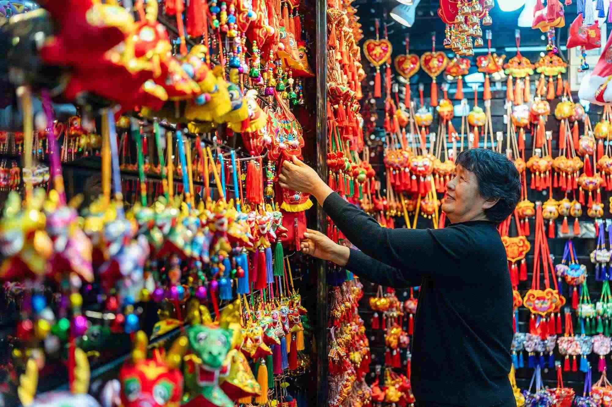 2023年12月11日，金華義烏國(guó)際商貿(mào)城，龍年喜慶用品掛滿攤位，顧客正在挑選中。