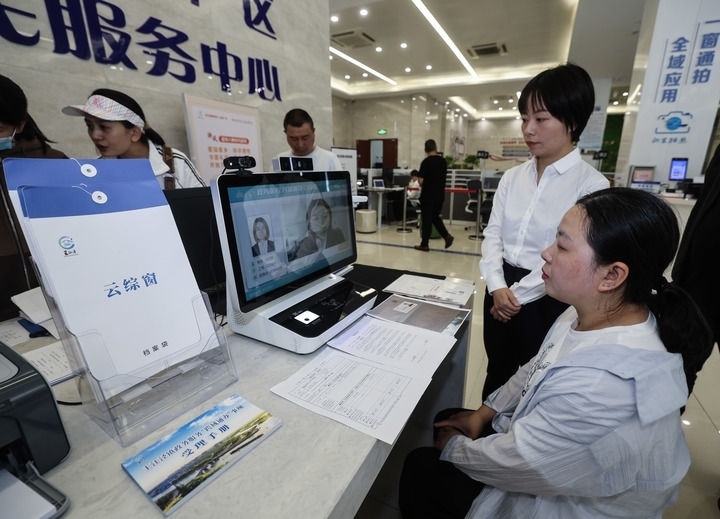 在浙江省嘉興市秀洲區(qū)王江涇鎮(zhèn)便民服務(wù)中心的“跨域通辦·云綜窗”窗口，辦理開(kāi)業(yè)登記的個(gè)體工商戶（右一）通過(guò)該系統(tǒng)與江蘇省蘇州市吳江區(qū)盛澤鎮(zhèn)行政審批局工作人員視頻連線，進(jìn)行身份讀取及材料線上審核（2024年5月9日攝）。新華社記者 徐昱 攝
