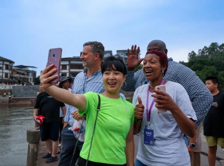 2024“一帶一路”媒體合作論壇聯(lián)合采訪調(diào)研行成員在樂山蘇稽古鎮(zhèn)與游客合影留念。本報(bào)記者 伊霄攝